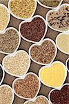 Healthy grain and cereal food selection in heart shaped porcelain bowls over hessian background.
