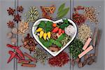 Spice and herb selection in a heart shaped dish and loose over wooden grey  background.