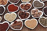 Spice selection in heart shaped porcelain dishes over old oak background.