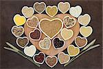 Grain food selection on a heart shaped wooden board and in porcelain bowls with wheat ears over lokta paper background.