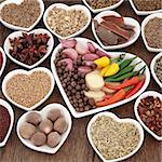 Herb and spice ingredients in heart shaped porcelain dishes over old oak background.