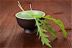 Fresh arugula leaves in black cup on dark wooden background. Culinary herbs concept.