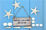 Gone to the beach sign with starfish, cockle and turritella seashells over wooden blue background.