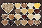 Grain and cereal food selection in heart shaped porcelain bowls over lokta paper background. Tricolour quinoia in large dish.