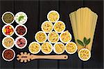 Italian pasta and mediterranean food ingredients in porcelain bowls over dark wood background.