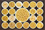 Large pasta dried food selection in round bowls over brown background.