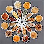 Large savoury snack selection in porcelain dishes over grey wooden background.