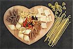 Dried pasta food selection on a heart shaped wooden board.