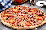Pizza with tomatoes, ham and mushrooms on a table