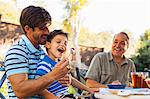 Father feeding son on lap, grandfather in background