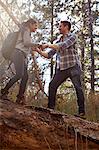 Young man giving girlfriend a helping hand on fallen tree in forest, Los Angeles, California, USA