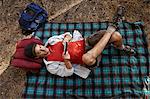Overhead view of young male camper lying on picnic blanket in forest, Los Angeles, California, USA