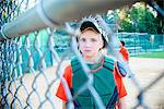 Young girl wearing baseball kit, looking through fence