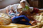 Three young children relaxing on bed using digital tablet