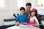 Mature man reading storybook to son and daughter on sofa