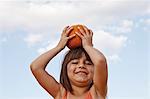 Low angle portrait of girl holding up pumpkin on her head