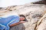 Boy covered with blanket sleeping on rock