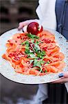 Person holding tray with smoked salmon and pomegranate seeds