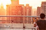 Woman with baby on roof, cityscape at sunset on background