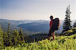 Man backpacking in the mountains, walking on a ridge overlooking a valley.