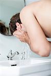 Man washing face in bathroom sink