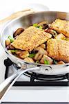 Cornmeal crusted trout fillets in a skillet with potatoes, mushrooms and green onions on a gas stove, studio shot