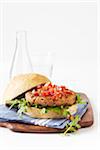 Salsa topped burger on a whole wheat bun, on cutting board with cloth napkin, studio shot on white background