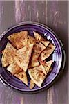 Purple plate filled with spiced whole-wheat pita chips, studio shot on purple background