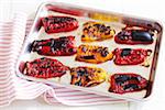 Roasted yellow and red peppers on a baking pan with a red striped napkin, studio shot on white background