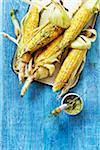 Grilled, corn on the cob with basting brush and herb butter, studio shot on blue background