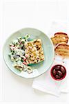 Lemon Cod with Greek Salad on a green plate, with Bread and Olives in bowl on cloth napkin, studio shot on white background