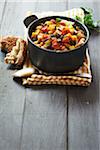 Tofu chilli in pot, with crusty bread on a gray, wooden table, studio shot