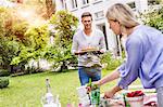 Mid adult man carrying cake on cake stand, walking towards garden table