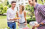 Group of friends setting up garden party, mid adult man carrying cake