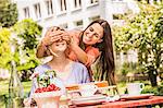 Two female friends in garden, one coverings the others eyes with hands