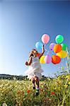 Girl jumping for joy with colorful balloons in wildflower meadow, Majorca, Spain