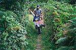 Mid adult man pushing wheelbarrow full of boys in garden