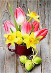 Bunch with Yellow Daffodils and Magenta Tulips in Watering Can with Colored Easter Eggs closeup on Wooden background