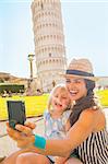 Happy mother and baby girl making selfie in front of leaning tower of pisa, tuscany, italy