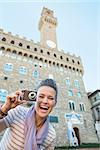Portrait of smiling young woman with photo camera in front of palazzo vecchio in florence, italy