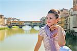 Young woman sitting on bridge overlooking ponte vecchio in florence, italy and looking into distance