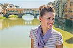 Happy young woman sitting on bridge overlooking ponte vecchio in florence, italy