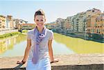 Happy young woman sitting on bridge overlooking ponte vecchio in florence, italy