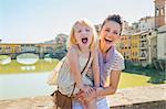 Portrait of smiling mother and baby girl standing on bridge overlooking ponte vecchio in florence, italy