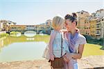 Happy mother and baby girl hugging on bridge overlooking ponte vecchio in florence, italy