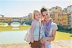 Portrait of happy mother and baby girl standing on bridge overlooking ponte vecchio in florence, italy