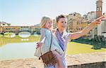 Happy mother and baby girl standing on bridge overlooking ponte vecchio in florence, italy and pointing