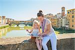 Mother and baby girl sitting on bridge overlooking ponte vecchio in florence, italy and looking at map
