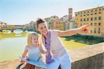 Happy mother and baby girl with map sitting on bridge overlooking ponte vecchio in florence, italy and pointing