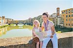 Happy mother and baby girl with map sitting on bridge overlooking ponte vecchio in florence, italy
